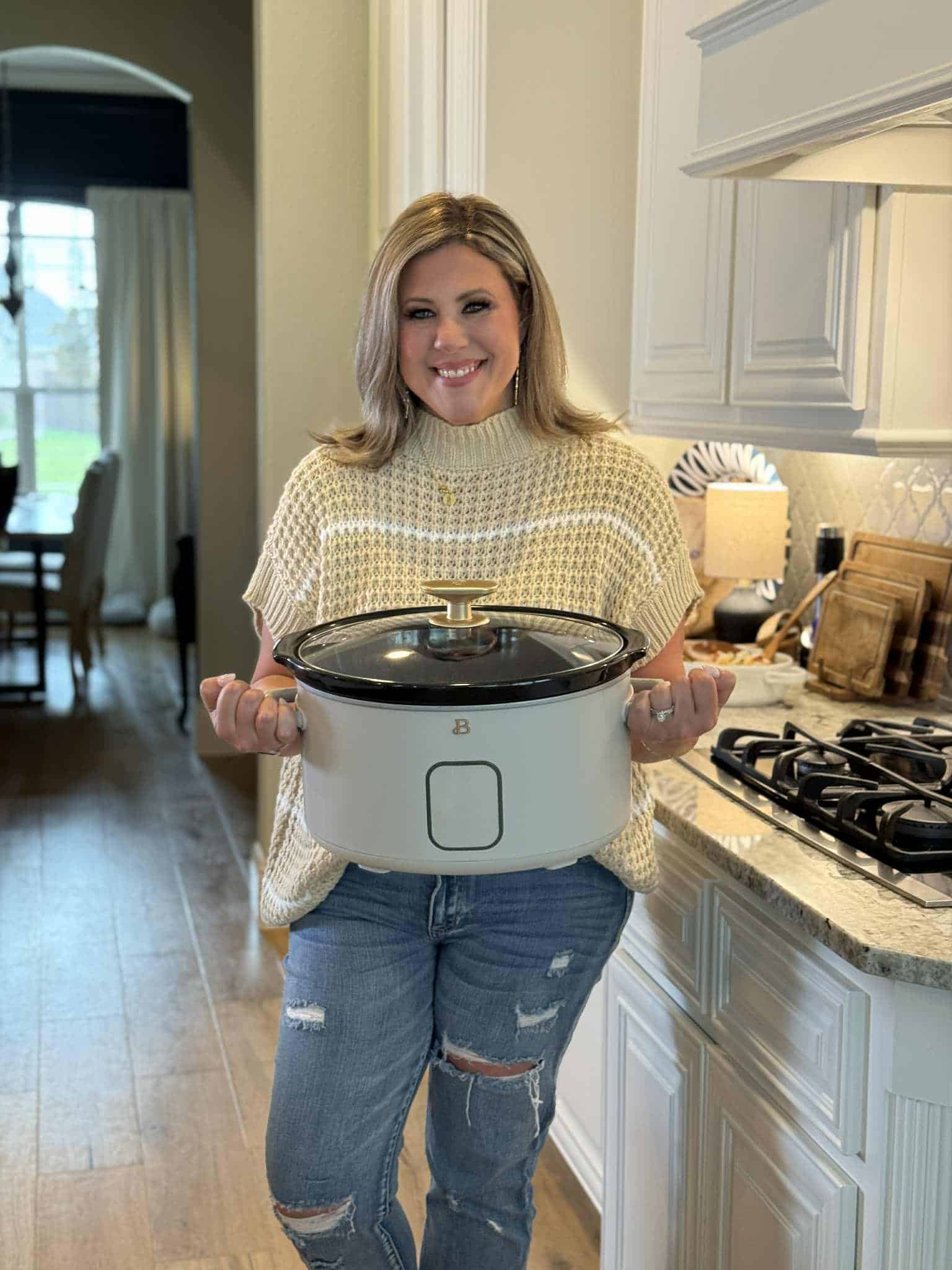 Woman holding a slow cooker in a bright, modern kitchen.