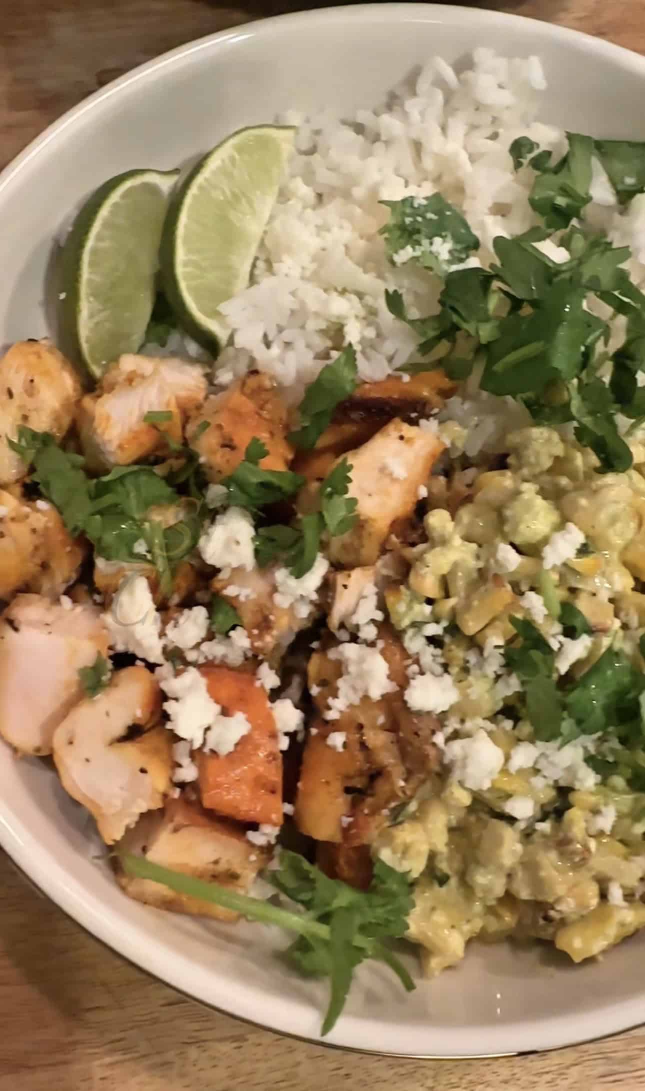 Street Corn Chicken Bowl with seasoned Sazón chicken, rice, sweet corn tossed in cilantro sauce, cotija cheese, avocado slices, and fresh cilantro served in a white bowl.