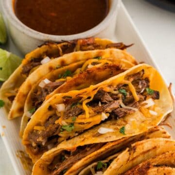 Beef tacos filled with seasoned meat, topped with shredded cheese and fresh herbs, served with a sid.