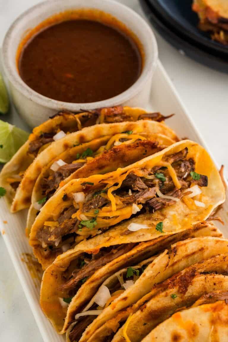 Beef tacos filled with seasoned meat, topped with shredded cheese and fresh herbs, served with a sid.