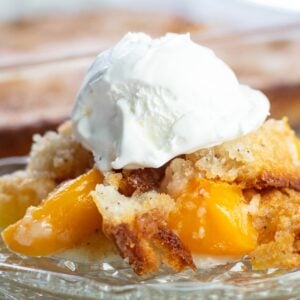 Creamy peach cobbler with a dollop of whipped cream on top, served in a glass dish. Perfect for summ.