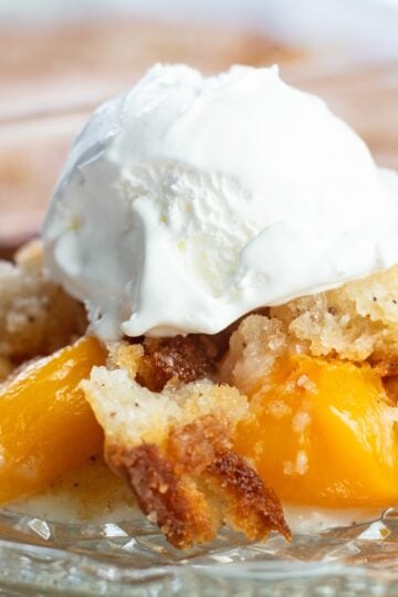 Creamy peach cobbler with a dollop of whipped cream on top, served in a glass dish. Perfect for summ.