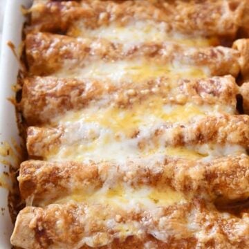 Cheesy baked enchiladas in a white baking dish, topped with melted cheese and sauce. Perfect for a f.