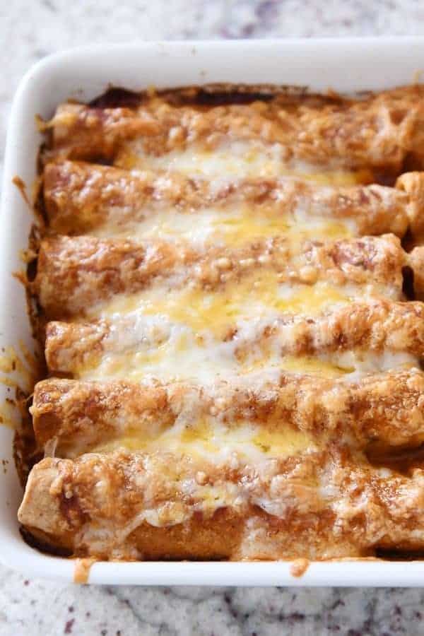 Cheesy baked enchiladas in a white baking dish, topped with melted cheese and sauce. Perfect for a f.