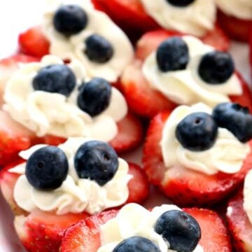 Red, white and blue strawberry cheesecake bites made with fresh strawberries, creamy cheesecake filling, and blueberries on a white serving platter.
