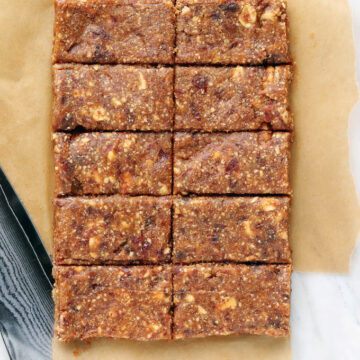 Stacked 2 Ingredient Cashew Date Bars on a white plate with whole cashews and Medjool dates in the background. These no-bake healthy snack bars are naturally sweetened, easy to make in a food processor, and perfect for meal prep, post-workout snacks, and road trips.