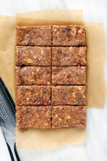Stacked 2 Ingredient Cashew Date Bars on a white plate with whole cashews and Medjool dates in the background. These no-bake healthy snack bars are naturally sweetened, easy to make in a food processor, and perfect for meal prep, post-workout snacks, and road trips.