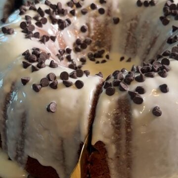 Easy Cannoli Cake topped with a sweet vanilla glaze, mini chocolate chips, powdered sugar, and chopped pistachios, served as an easy semi-homemade dessert.