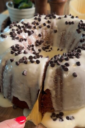 Easy Cannoli Cake topped with a sweet vanilla glaze, mini chocolate chips, powdered sugar, and chopped pistachios, served as an easy semi-homemade dessert.