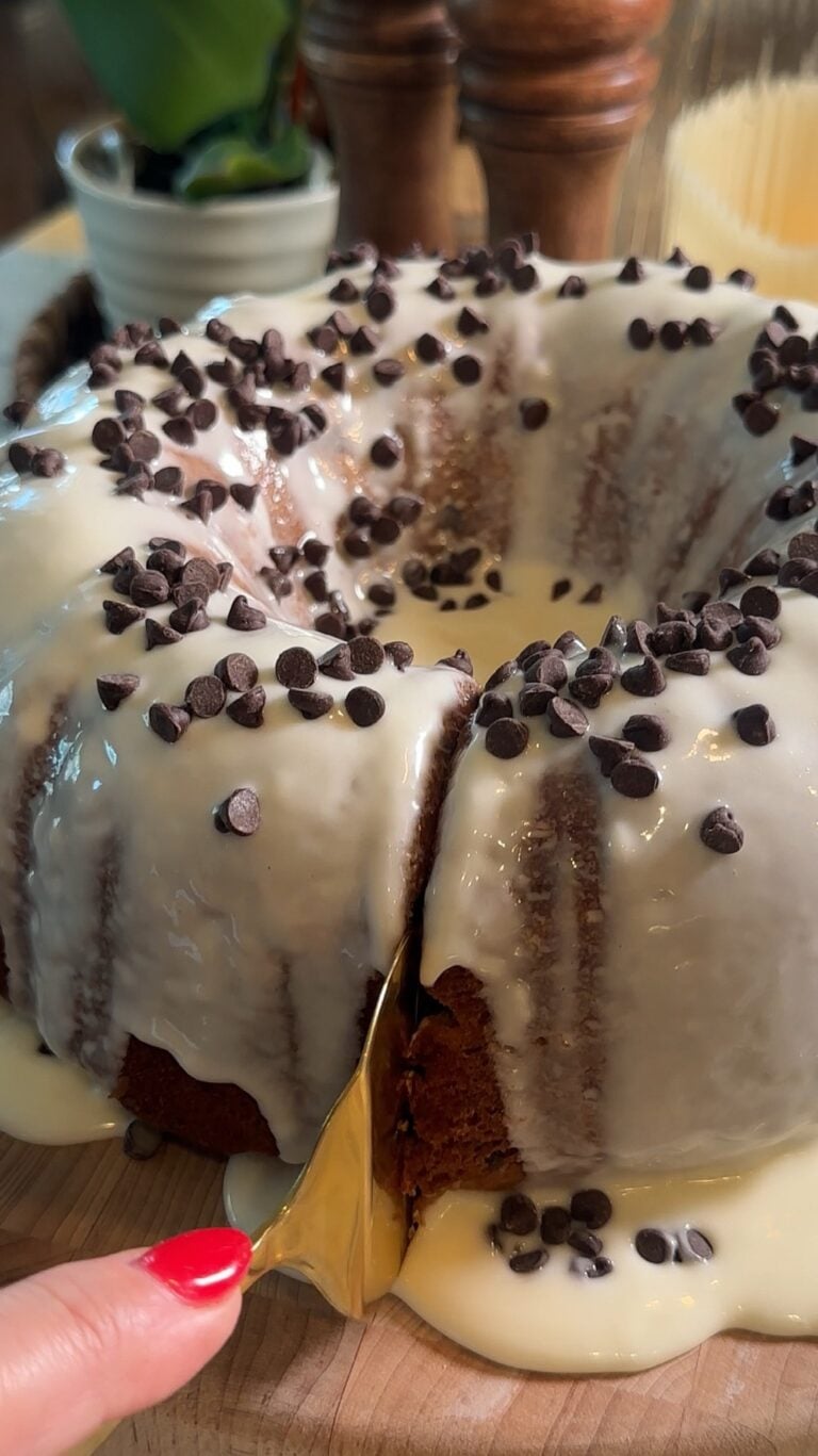 Easy Cannoli Cake topped with a sweet vanilla glaze, mini chocolate chips, powdered sugar, and chopped pistachios, served as an easy semi-homemade dessert.