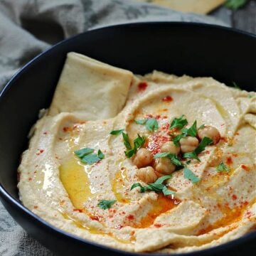 Creamy homemade garlic hummus topped with olive oil, chickpeas, and fresh herbs, served with pita bread for dipping.