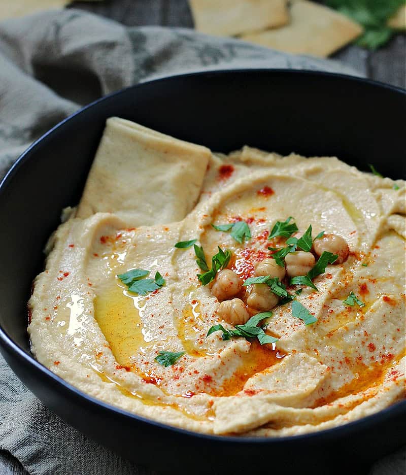 Creamy homemade garlic hummus topped with olive oil, chickpeas, and fresh herbs, served with pita bread for dipping.