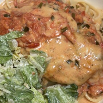 Creamy Tomato Chicken served over buttered pasta with blistered cherry tomatoes, mozzarella cheese, and fresh basil, and garlic scapes.