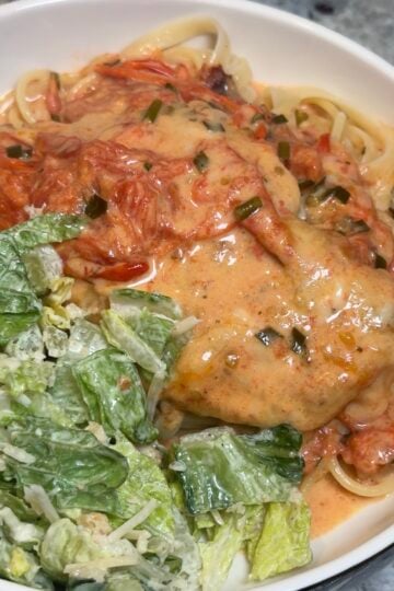 Creamy Tomato Chicken served over buttered pasta with blistered cherry tomatoes, mozzarella cheese, and fresh basil, and garlic scapes.