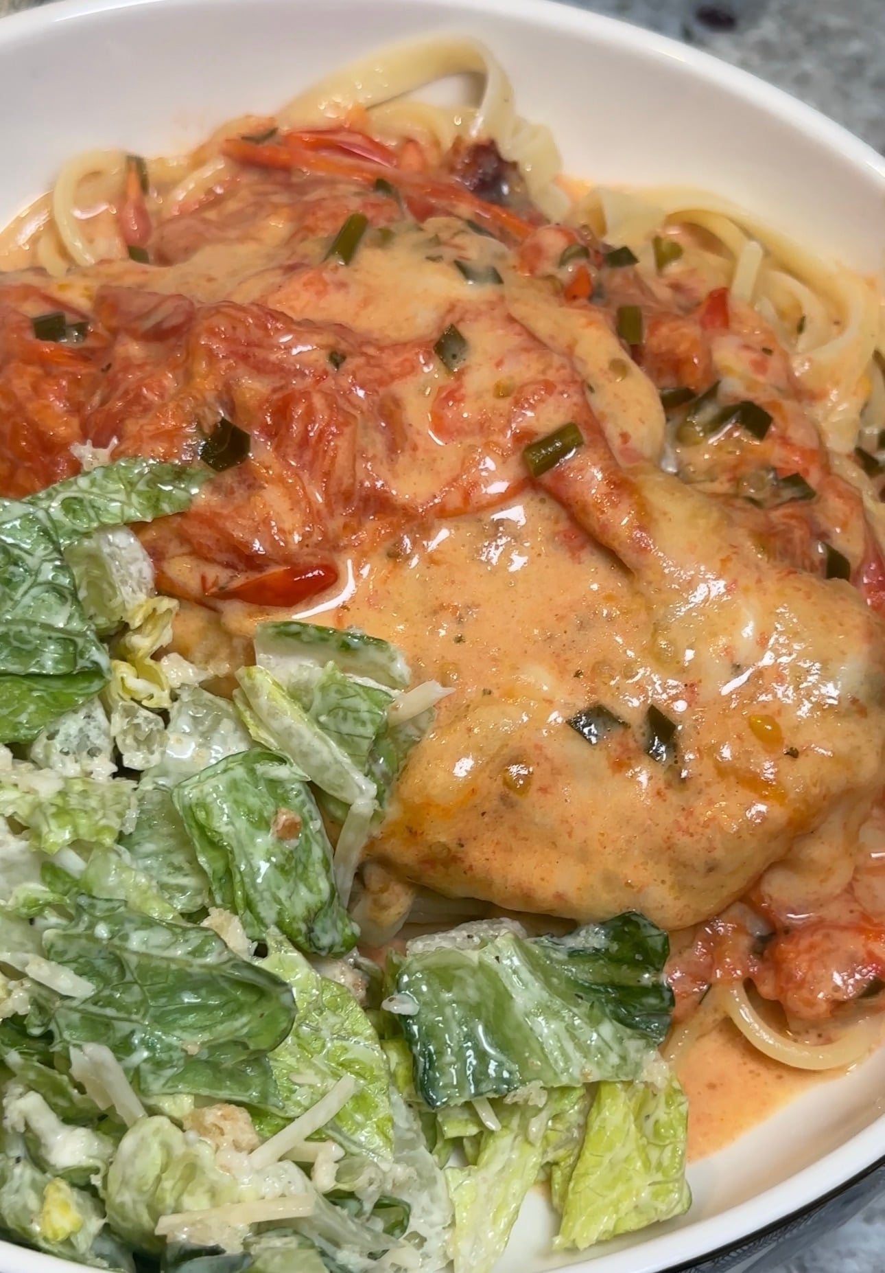 Creamy Tomato Chicken served over buttered pasta with blistered cherry tomatoes, mozzarella cheese, and fresh basil, and garlic scapes.