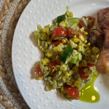 Corn & Tomato Orzo Pasta Salad with grilled corn, cherry tomatoes, cucumber, red onion, and garlic cilantro dressing served in a white bowl.