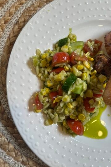 Corn & Tomato Orzo Pasta Salad with grilled corn, cherry tomatoes, cucumber, red onion, and garlic cilantro dressing served in a white bowl.