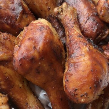 Smoked BBQ chicken drumsticks glazed with barbecue sauce on a white platter with fresh parsley.