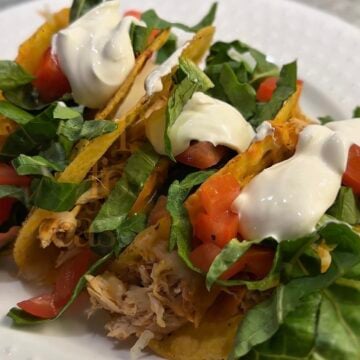 Crispy baked salsa chicken tacos filled with slow cooker shredded chicken, melted cheese, lettuce, tomatoes, avocado, and sour cream on a serving platter.