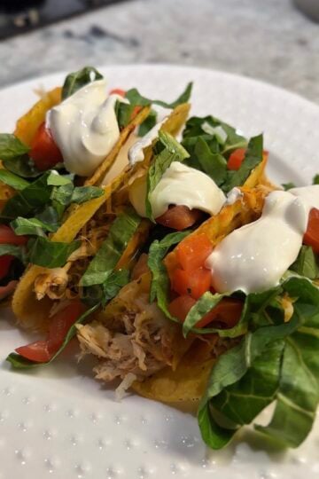 Crispy baked salsa chicken tacos filled with slow cooker shredded chicken, melted cheese, lettuce, tomatoes, avocado, and sour cream on a serving platter.