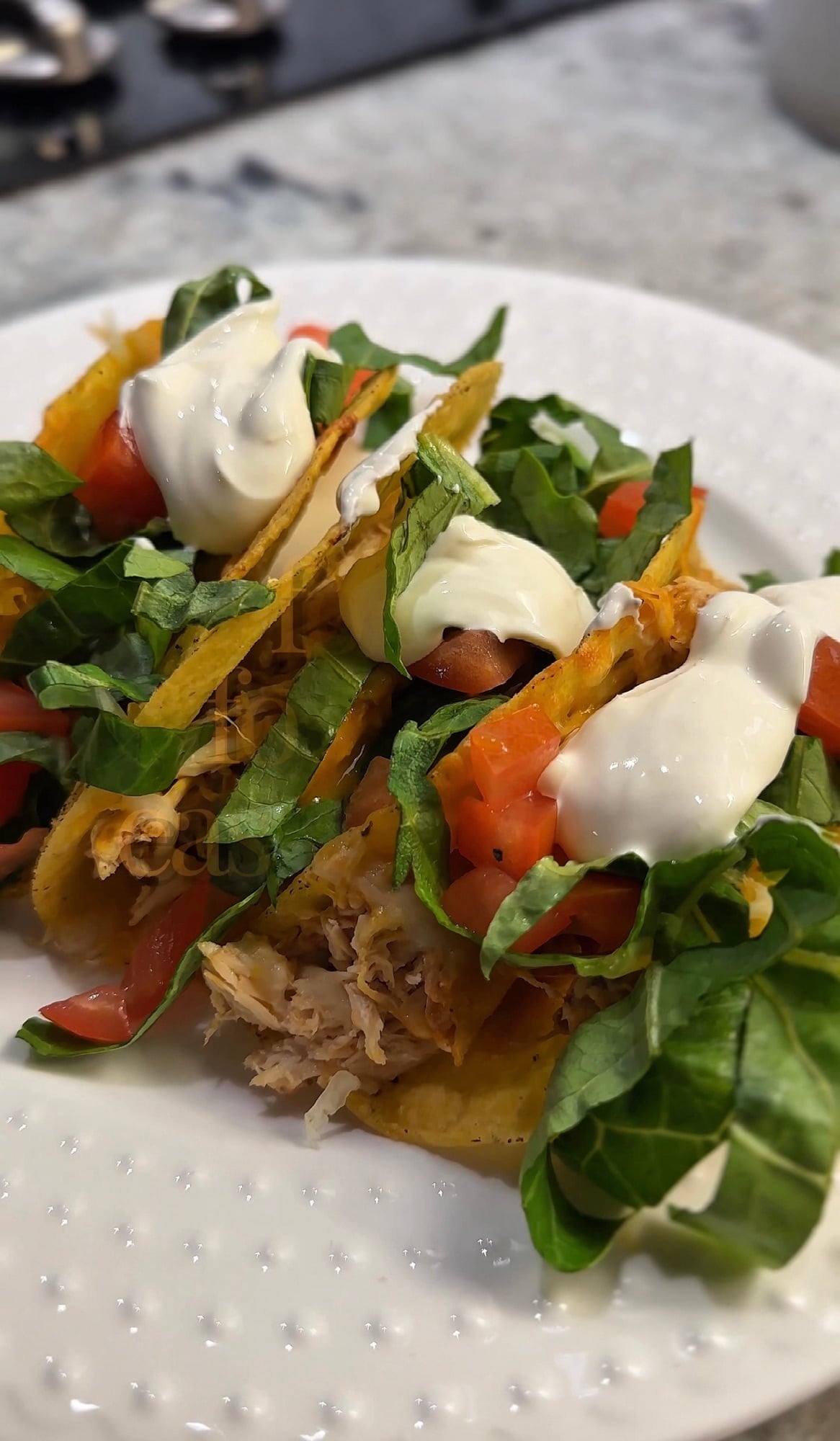 Crispy baked salsa chicken tacos filled with slow cooker shredded chicken, melted cheese, lettuce, tomatoes, avocado, and sour cream on a serving platter.
