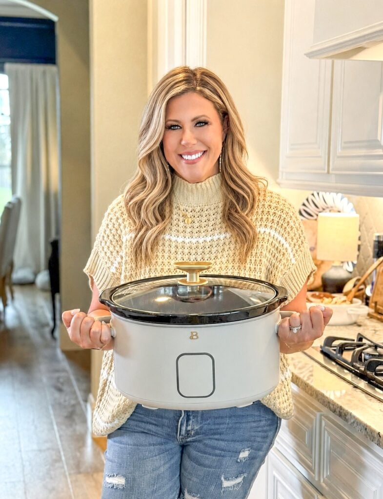 Lacey Watts holding a rustic serving platter of homemade comfort food in a bright farmhouse kitchen, sharing easy family recipes and entertaining inspiration.