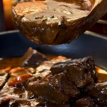 Beef bourguignon in a red Dutch oven with tender chunks of beef, mushrooms, pearl onions and carrots in a glossy red wine sauce