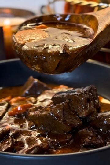 Beef bourguignon in a red Dutch oven with tender chunks of beef, mushrooms, pearl onions and carrots in a glossy red wine sauce
