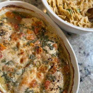Creamy high protein Tuscan chicken bake in a white baking dish topped with melted parmesan, diced tomatoes, and spinach