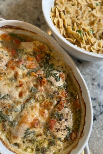 Creamy high protein Tuscan chicken bake in a white baking dish topped with melted parmesan, diced tomatoes, and spinach