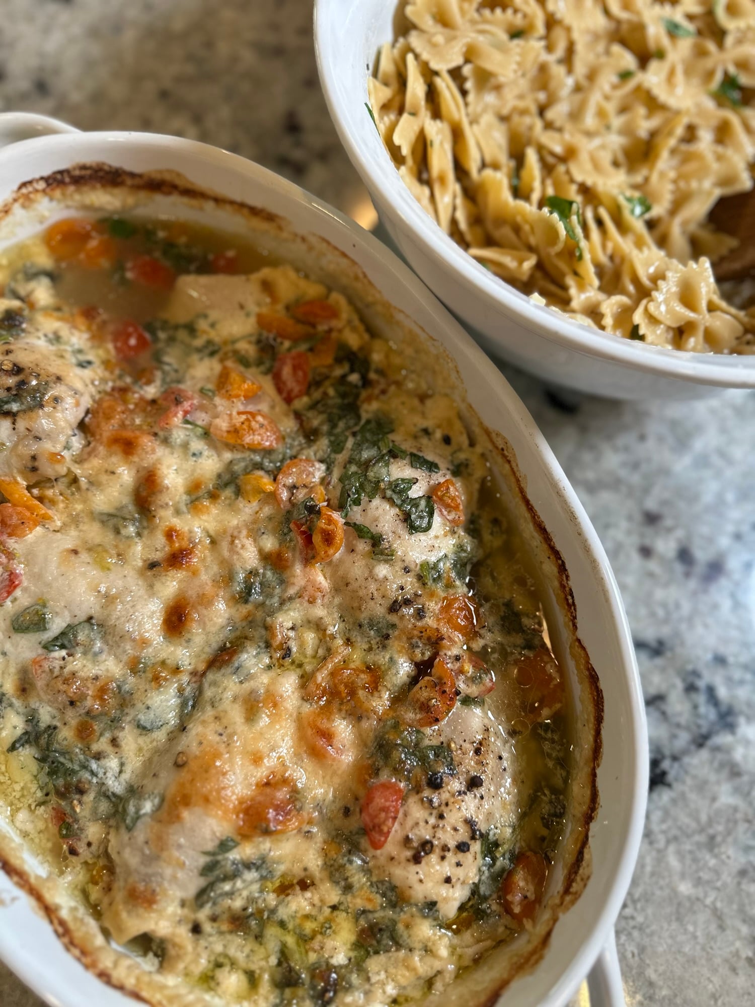 Creamy high protein Tuscan chicken bake in a white baking dish topped with melted parmesan, diced tomatoes, and spinach