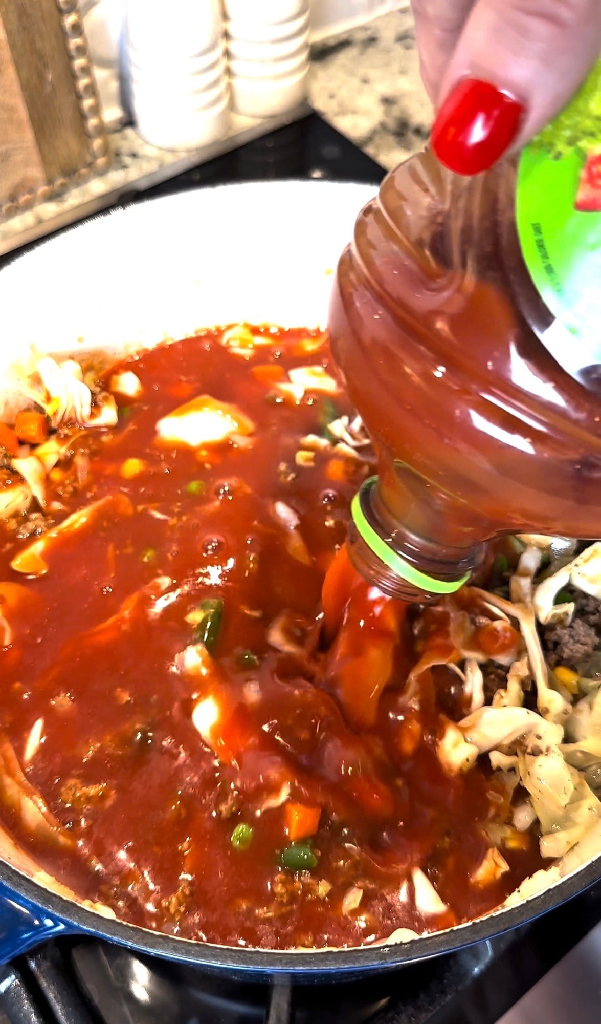 V8 vegetable juice being poured into a pot of homemade veggie beef soup with ground beef and vegetables.