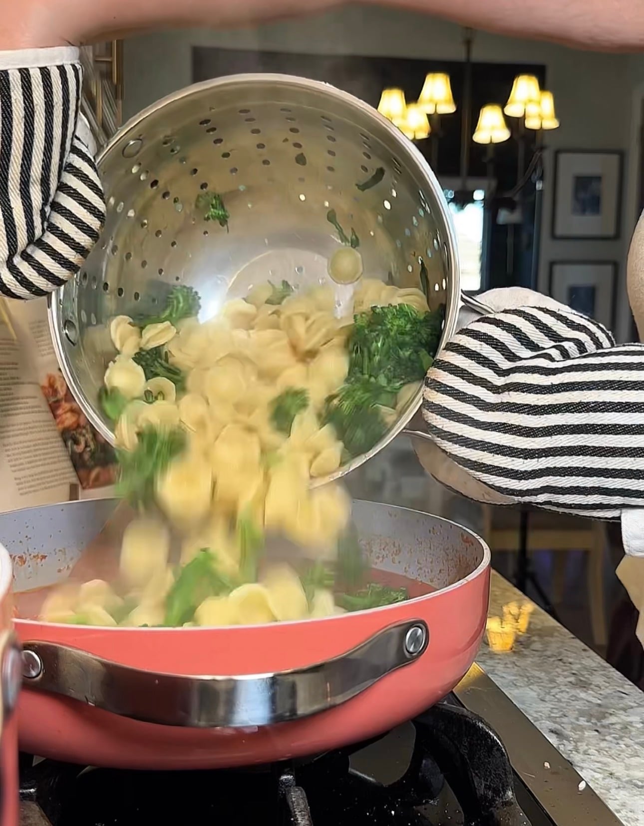 Cooked orecchiette and broccoli rabe being added to a pan of sausage and tomato sauce.