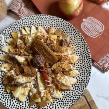 Honeycrisp apple nachos topped with caramel, white chocolate, crushed Biscoff cookies, chopped peanuts, and Ferrero Rocher candy.
