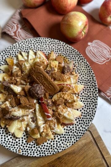 Honeycrisp apple nachos topped with caramel, white chocolate, crushed Biscoff cookies, chopped peanuts, and Ferrero Rocher candy.