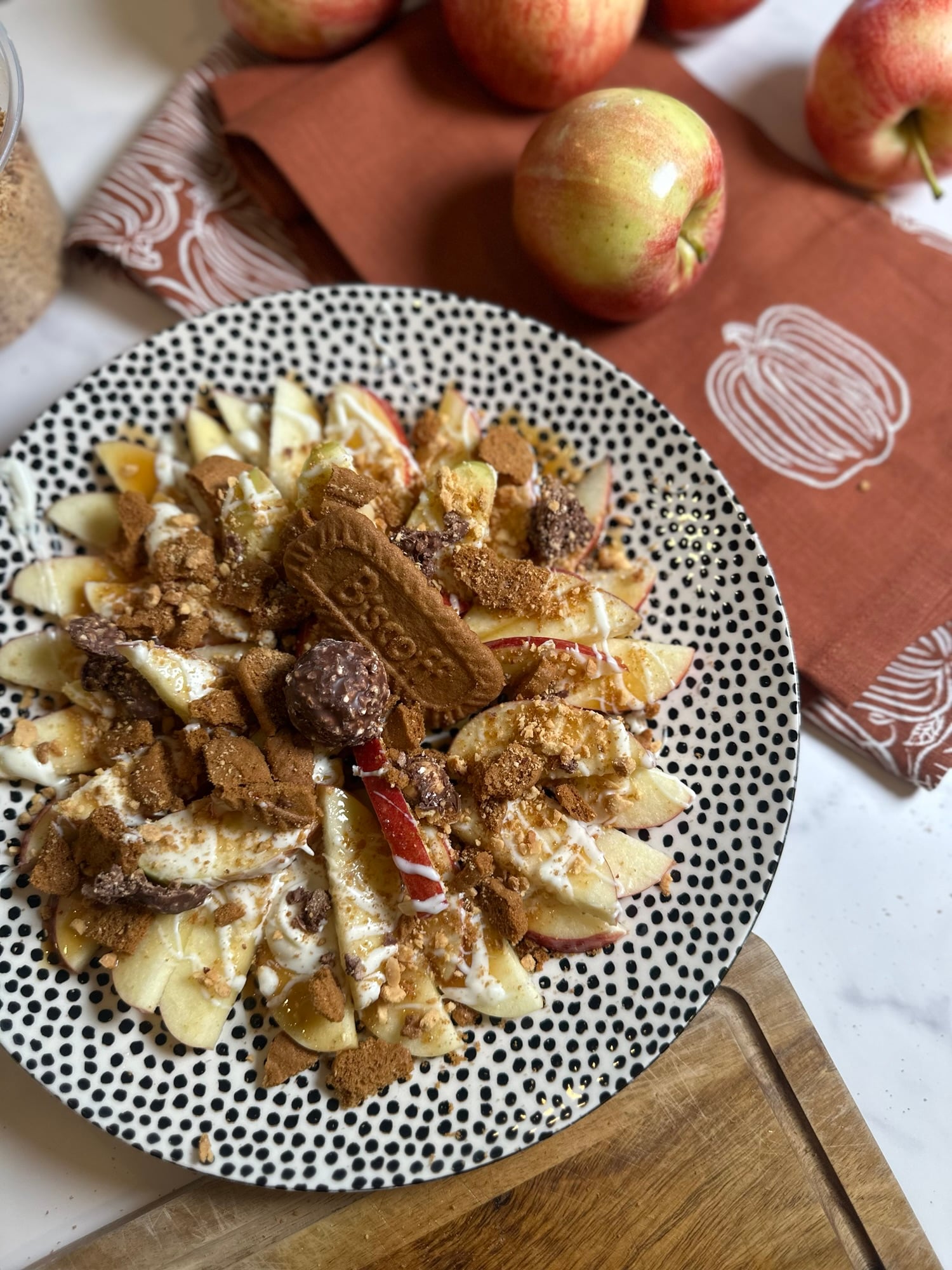 Honeycrisp apple nachos topped with caramel, white chocolate, crushed Biscoff cookies, chopped peanuts, and Ferrero Rocher candy.