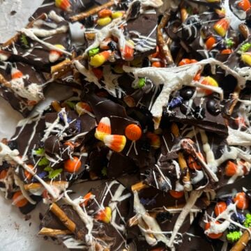 Halloween chocolate bark topped with pretzels, candy corn, colorful candies, white chocolate drizzle, and marshmallow spiderwebs.