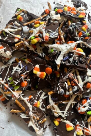 Halloween chocolate bark topped with pretzels, candy corn, colorful candies, white chocolate drizzle, and marshmallow spiderwebs.