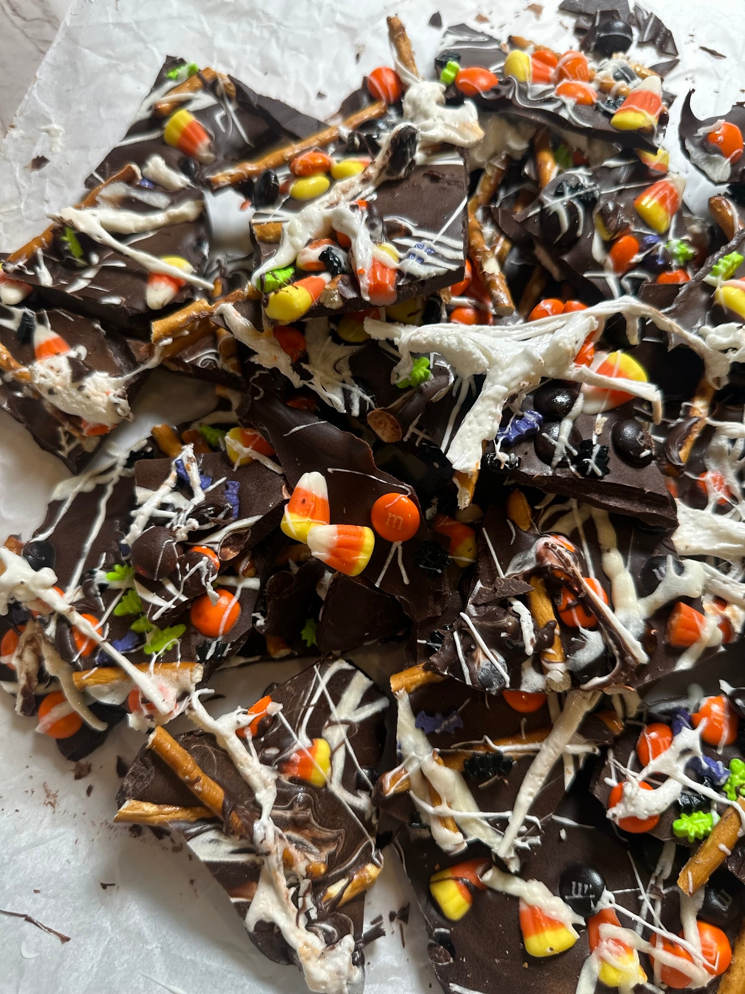Halloween chocolate bark topped with pretzels, candy corn, colorful candies, white chocolate drizzle, and marshmallow spiderwebs.