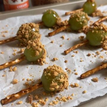 Green grapes dipped in caramel and chopped peanuts with pretzel sticks